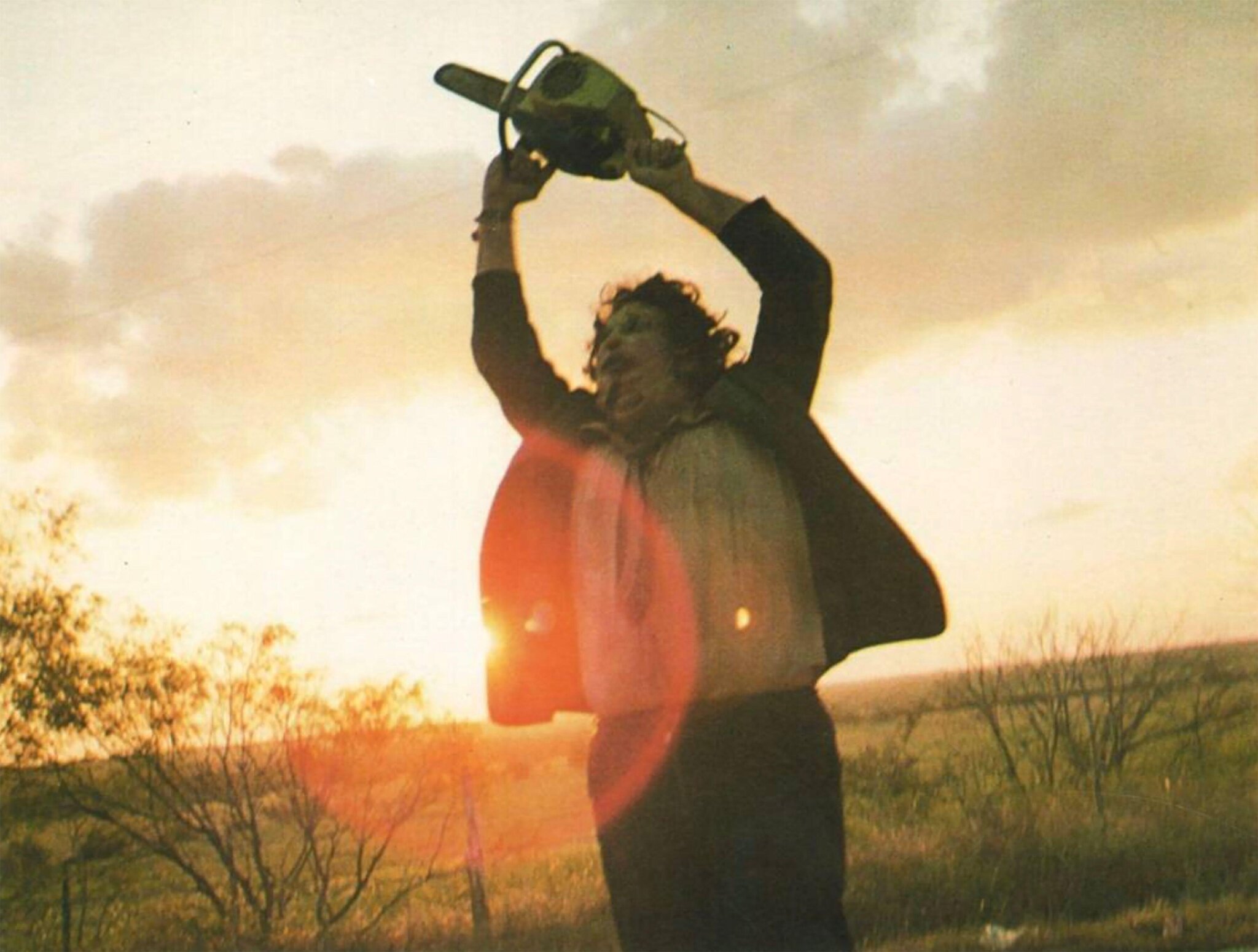 A person silhouetted against a sunset sky, holding a chainsaw above their head.